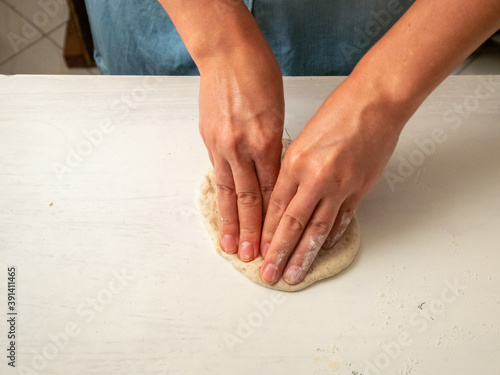 Woman in Blue Uniform Kneads Bread in a White Background