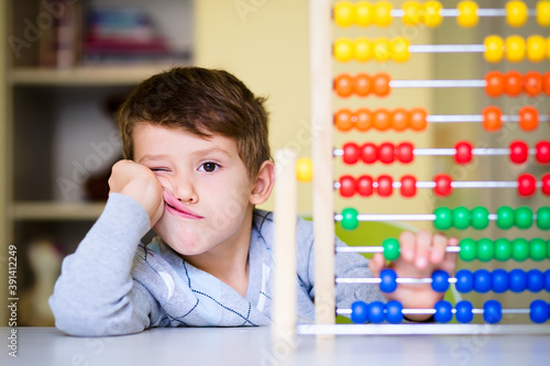 Caucasian toddler boy feeling bored and tired while playing with abacus at kindergarten photo