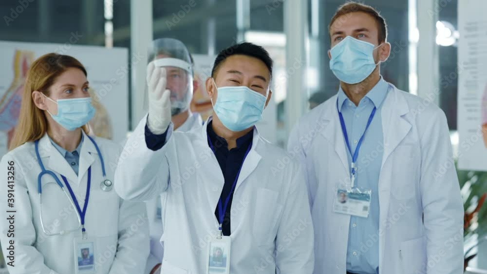 Diverse young doctors team communicating in medical office wearing masks agree to nee vaccination applauding successful meeting. Professional staff. Quarantine. Coronavirus. Diverse young doctors team communicating in medical office wearing masks agree to nee vaccination applauding successful meeting. Professional staff. Quarantine. Coronavirus.