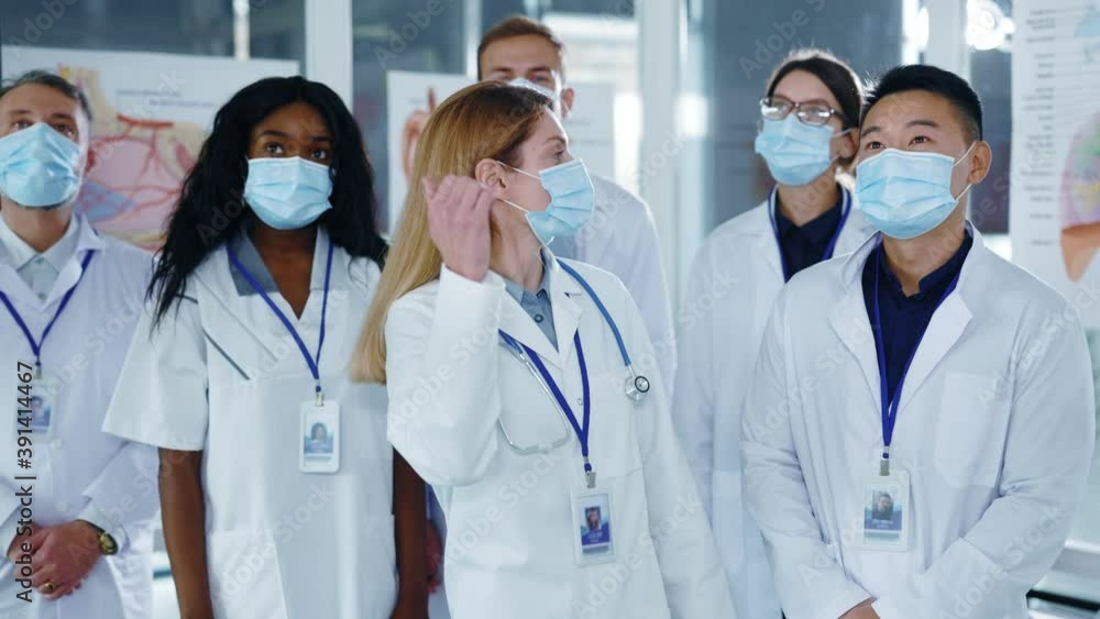 Professional multi-cultural group of medical workers wearing face masks against coronavirus looking at camera inside office environment applauding. Multi-ethnic staff. Hospitals. Professional multi-cultural group of medical workers wearing face masks against coronavirus looking at camera inside office environment applauding. Multi-ethnic staff. Hospitals.