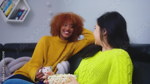 Multiracial friendship. Afican american black and asian woman eating popcorns gossiping and watching movies. Flirting and looking at each other. High quality 4k footage photo