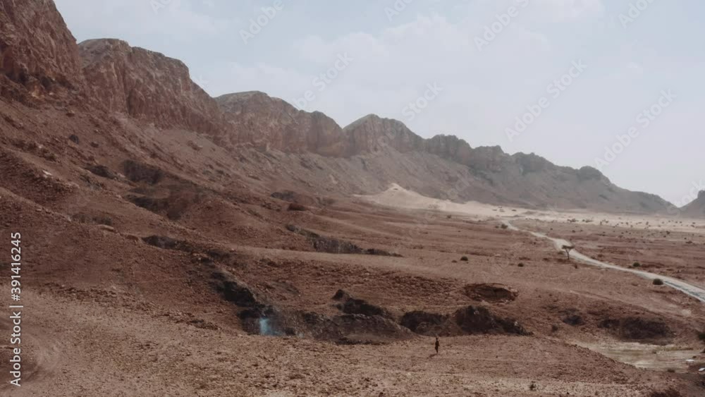 Man Walking Alone On The Arid Land By The Mountain - static shot Man Walking Alone On The Arid Land By The Mountain - static shot