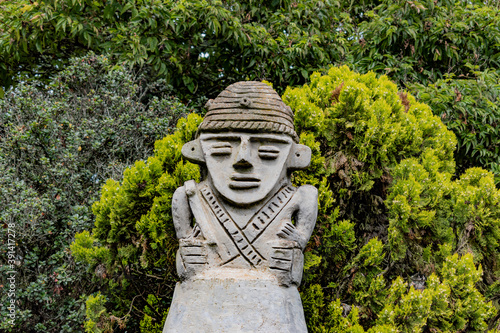 A picture of an antique muisca statue with some vegetation behind and beneath it. Photo taken at a small town. photo