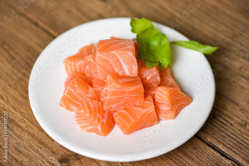 Raw salmon filet cube with herbs and spices on white plate on wooden background