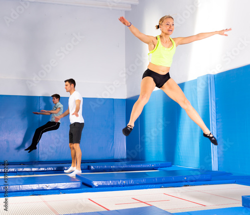 Young athletic woman exercising acrobatic elements in jump on trampoline in sports center..