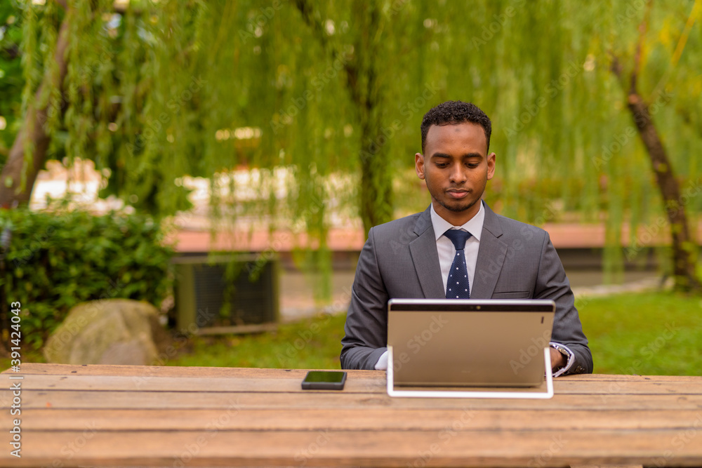African businessman sitting outdoors using laptop computer African businessman sitting outdoors using laptop computer