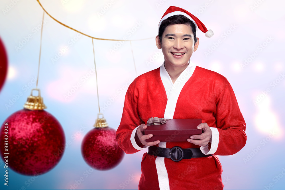 Εκτύπωση καμβά Asian man in Santa costume holding gift box with Christmas ornament background