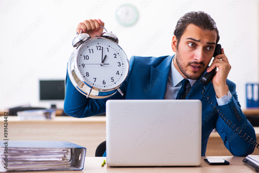 Young male employee in time management concept Young male employee in time management concept
