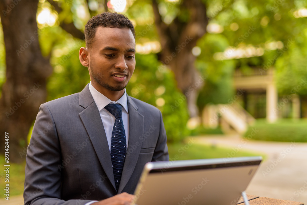 African businessman sitting outdoors using laptop computer while smiling African businessman sitting outdoors using laptop computer while smiling