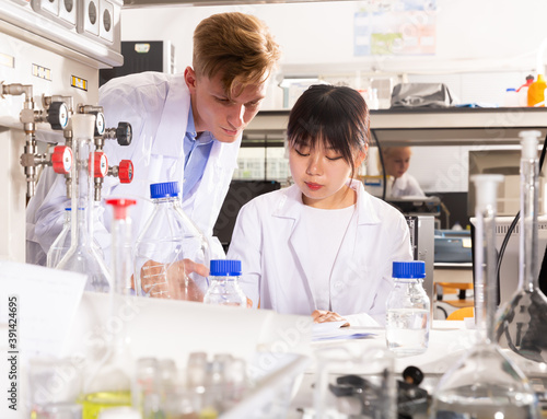 Positive Chinese female student noting results of research at chemical lab