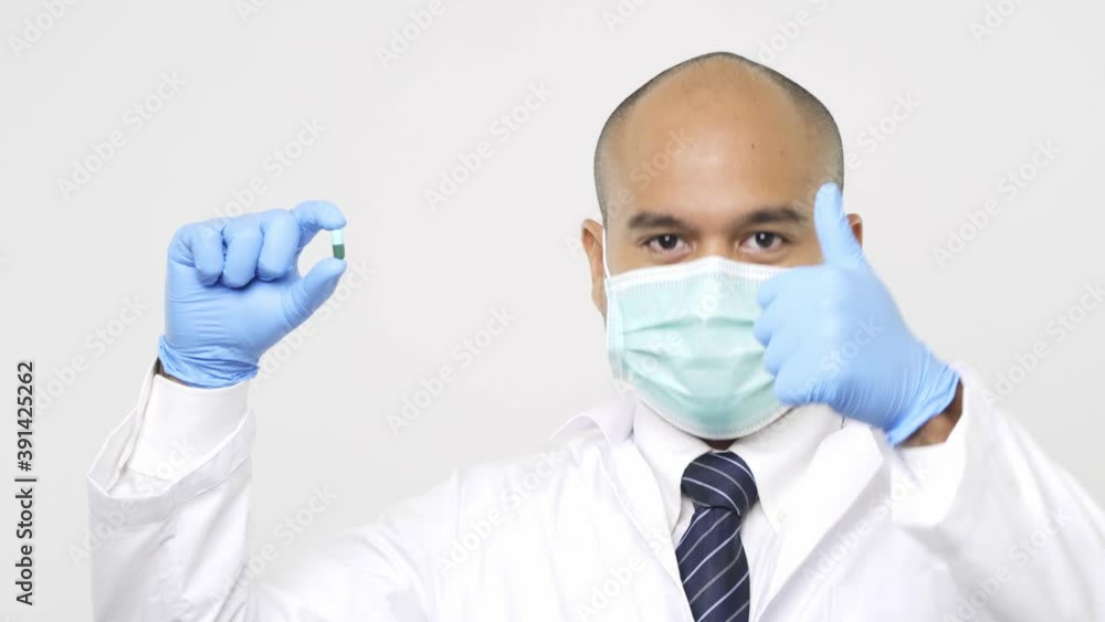 Young asian doctor in uniform put on a face mask holding a medicine with blue glove get thumb up on isolated white background. 4K Resolution. Young asian doctor in uniform put on a face mask holding a medicine with blue glove get thumb up on isolated white background. 4K Resolution.