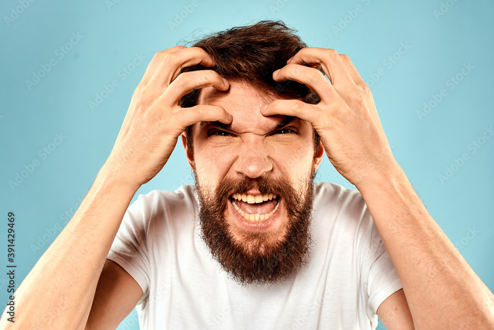 Bearded man in white T-shirt emotions gestures with hands displeased facial expression blue background Bearded man in white T-shirt emotions gestures with hands displeased facial expression blue background