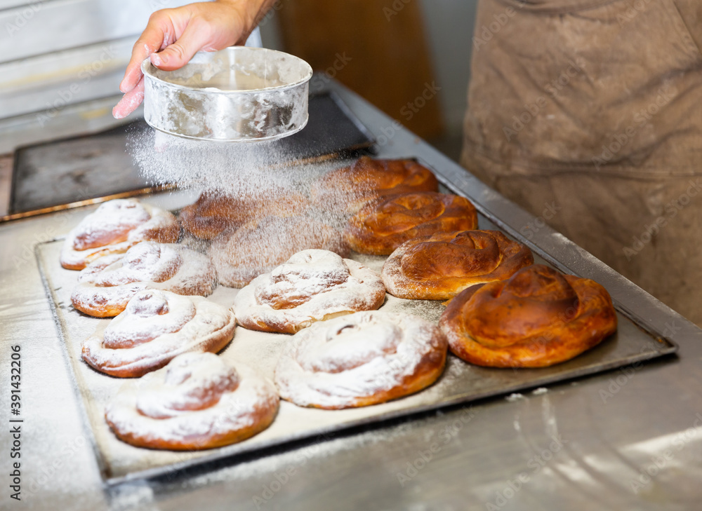Baker hands dusting freshly baked ensaimadas with powdered sugar in
