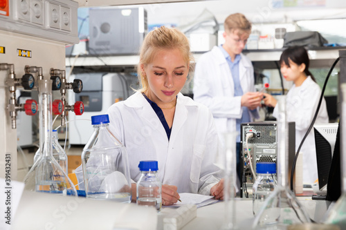Portrait of female scientist registering results of research in notebook at biochemical laboratory
