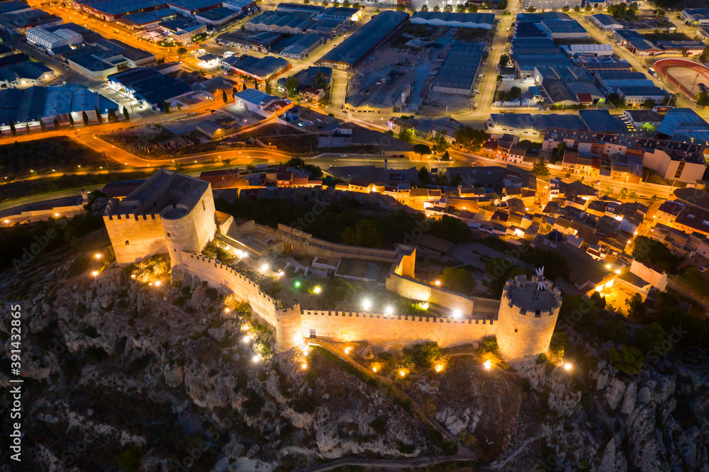 Aerial view of medieval fortified Castalla Castle on top of stone hill on background with townscape in twilight, province of Alicante, Spain..