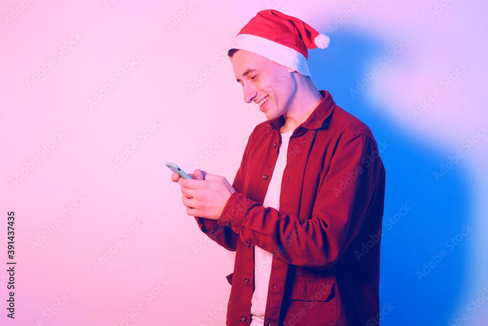 A man in a santa hat in neon light. A guy with a phone in his hands is texting or looking for something on the Internet. New Year's and Christmas. A man in a santa hat in neon light. A guy with a phone in his hands is texting or looking for something on the Internet. New Year's and Christmas.