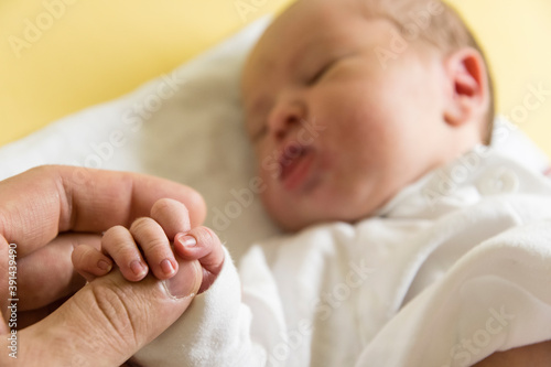 A man holding the fingers of a newborn with the baby's face in the background.