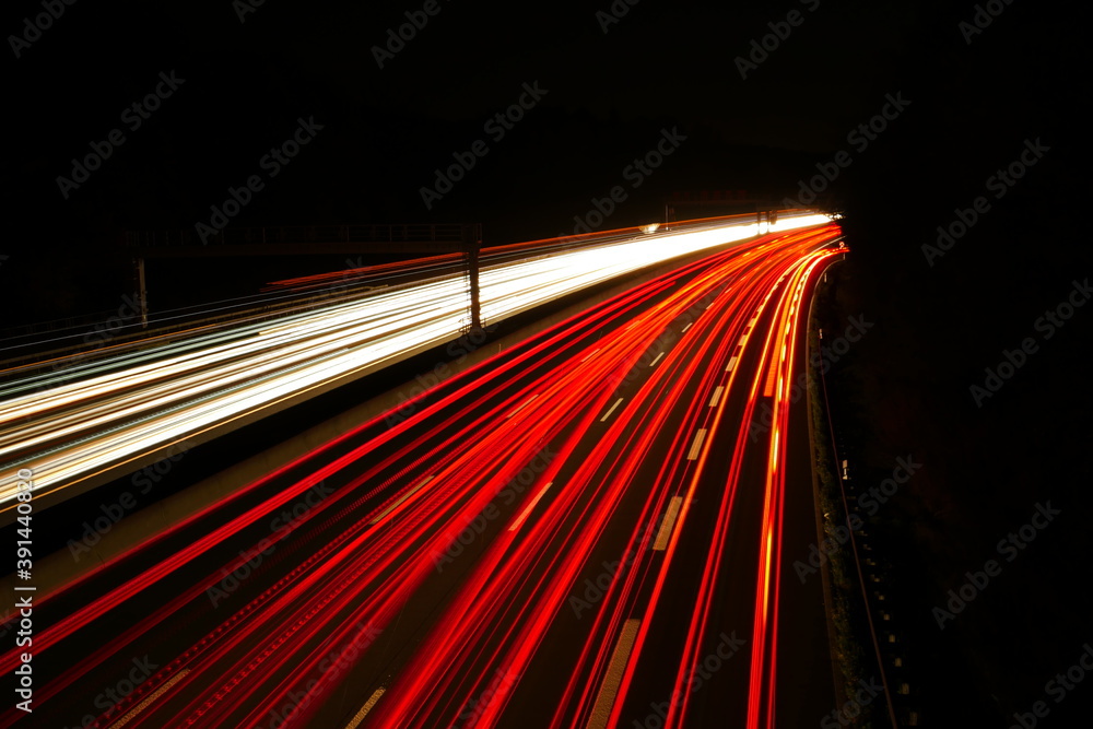 highway traffic at night in a right curve with red white yellow lights and a toll bridge