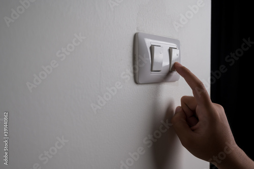 Earth Hour, Close up male hand turn off the light to saving electrical energy. Finger pushing light switch turn on or off. White switch with copy space at home. photo