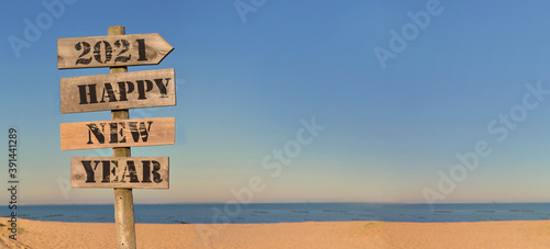 2021 happy new year writing on a wooden post sign on the beach in panoramic view
