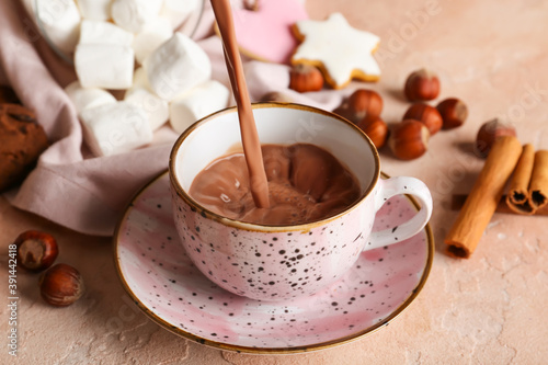 Pouring of hot cacao drink into cup on color background