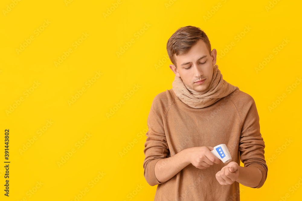 Young man measuring his temperature on color background Young man measuring his temperature on color background
