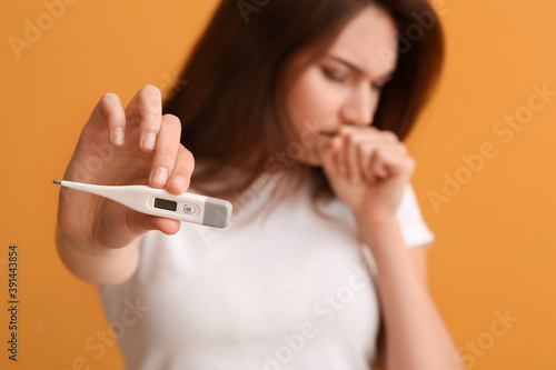 Ill young woman with thermometer on color background