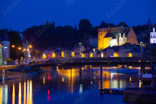 Scenic view of lighted ancient Laval castle on banks of Mayenne river at summer dusk, France