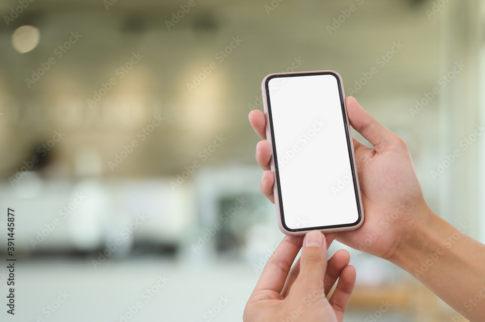 Cropped shot of man hands holding smart phone with white screen on blured living room background. Cropped shot of man hands holding smart phone with white screen on blured living room background.