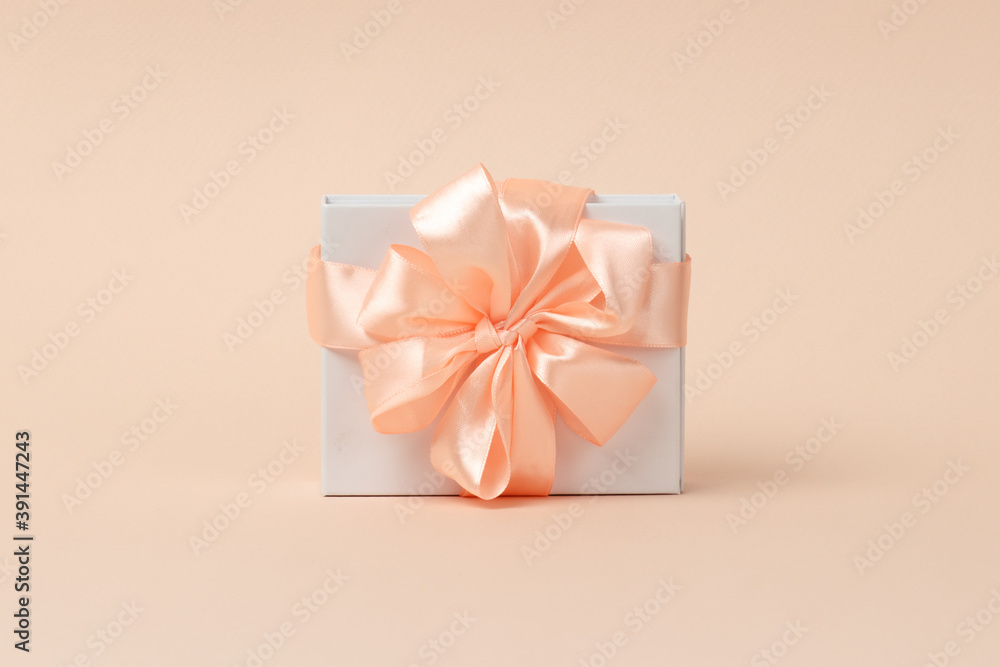 Valentine's Day background. Happy Womens day template design. Decorative white gift box with peach bow on pastel coral background. Object in the center. Close-up Valentine's Day background. Happy Womens day template design. Decorative white gift box with peach bow on pastel coral background. Object in the center. Close-up