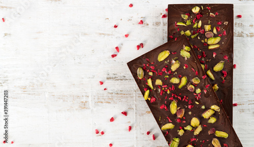 Two dark chocolate bars with sublimated raspberries and pistachios on white wooden background. Copy space. Top view. Horizontal orientation.