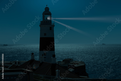 At night at the red and white trinity lighthouse on the British territory of Gibraltar. The moonlight illuminates the Strait of Gibraltar with some ships.