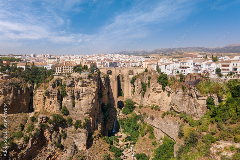 Impressive panoramic view from the air of the Andalusian city of Ronda with sunshine and blue skies in summer. In the middle the famous bridge with a waterfall.
