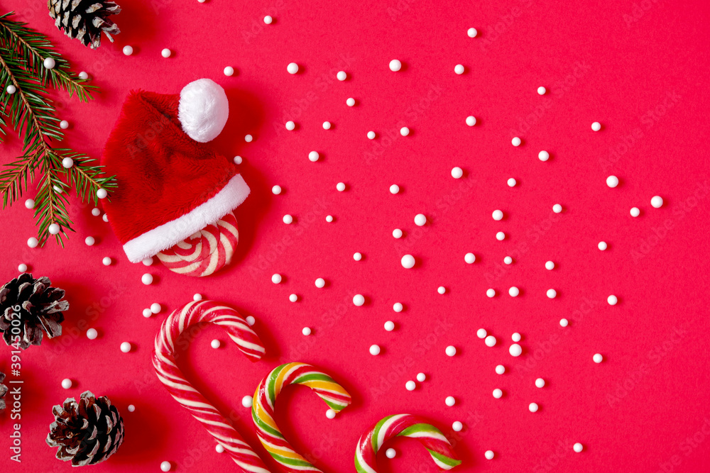 Christmas or New Year red background, Santa Claus hat, caramel cane, fir branches, cones, space for text, minimalism Christmas or New Year red background, Santa Claus hat, caramel cane, fir branches, cones, space for text, minimalism