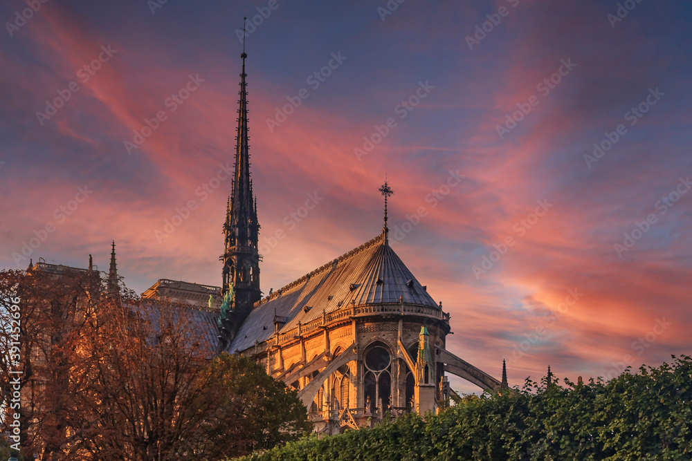 Eastern facade of Notre Dame de Paris Cathedral with flying buttresses and ornate gothic spire colored by the warm light of sunset in Paris, France