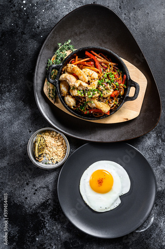 Udon stir fry noodles with chicken and vegetables in pan. Black background. Top view