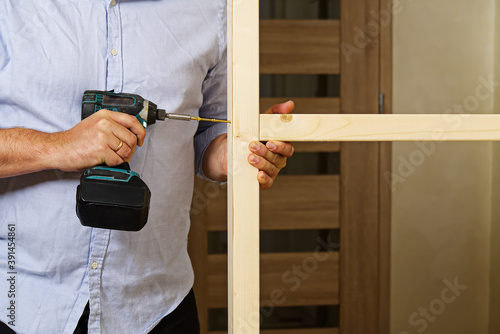 A man fastens two wooden beams with a self-tapping screw. The joiner wraps the screw with a screwdriver. Construction of a timber frame for plasterboard