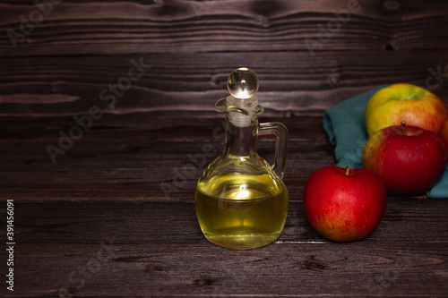 Apple cider vinegar in a glass decanter on a dark wooden table. Apples nearby. Free space.