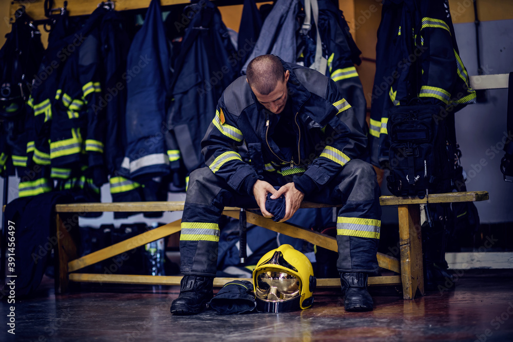 Young attractive fireman in protective uniform sitting in fire station and waiting for other firemen. He is prepared for action. Young attractive fireman in protective uniform sitting in fire station and waiting for other firemen. He is prepared for action.