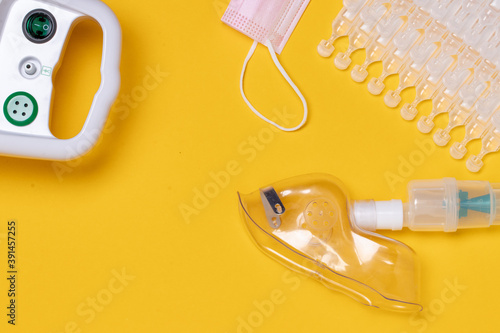 Coronavirus protective measures. Closeup of a inhaler device with medical face mask or nebulizer for treatment of the respiratory tract, sodium chloride in ampoules and a surgical mask flat lay on ye photo