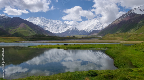 View of Achik Tash basecamp of Lenin Peak aka Ibn Sina peak with reflection in lake in snow-capped Trans Alay or Trans Alai mountain range, southern Kyrgyzstan 