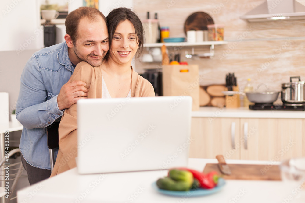 Romantic couple using laptop in kitchen searching breakfast recipe. Happy loving cheerful romantic in love couple at home using modern wifi wireless internet technology Romantic couple using laptop in kitchen searching breakfast recipe. Happy loving cheerful romantic in love couple at home using modern wifi wireless internet technology