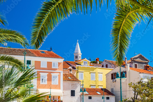 Beautiful town of Mali Losinj on the island of Losinj, Adriatic coast in Croatia, cathedral tower and city center, view through the palm leaves