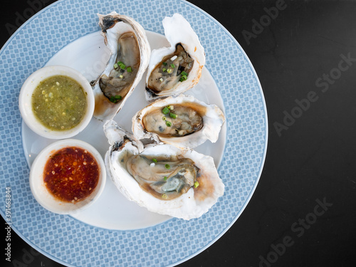 Fresh raw oysters recipe with Thai green seafood and red chili sauce in blue pattern platter on modern black table at buffet restaurant