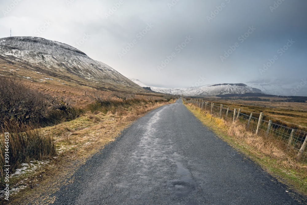 Empty small road in a mountains on a winter day. Peaks covered with snow. Clear sky. Gleniff Horseshoe Drive, county Sligo, Ireland. Popular tourist route and destination