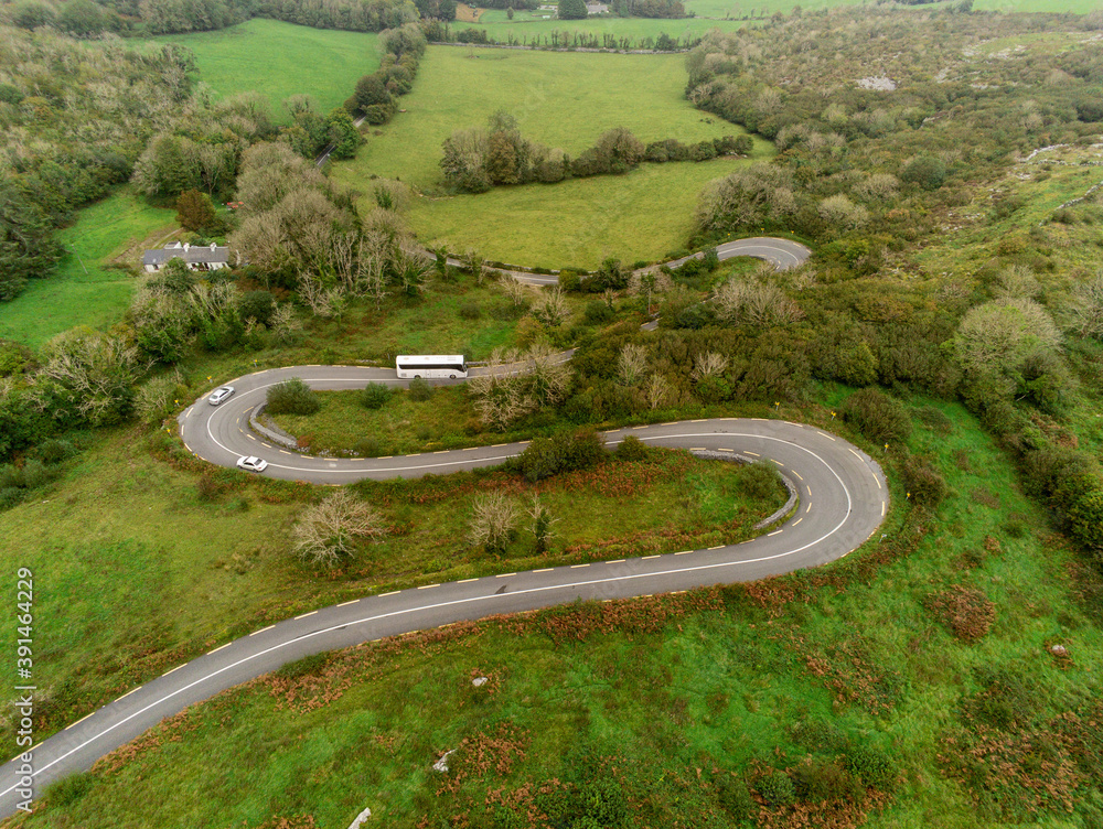 Winding narrow road on a hill in Burren, Ireland. Aerial drone view. Green fields and small trees around the pass. Winding narrow road on a hill in Burren, Ireland. Aerial drone view. Green fields and small trees around the pass.