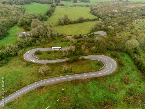 Winding narrow road on a hill in Burren, Ireland. Aerial drone view. Green fields and small trees around the pass.