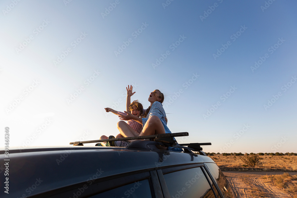 Teenage girl and her younger brother on top of SUV on desert road, Galisteo Basin, Santa Fe Teenage girl and her younger brother on top of SUV on desert road, Galisteo Basin, Santa Fe
