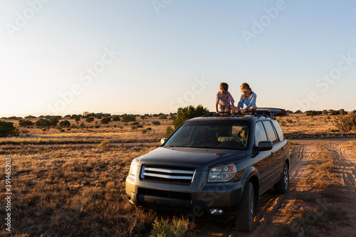 Teenage girl and her younger brother  on top of SUV on desert road
