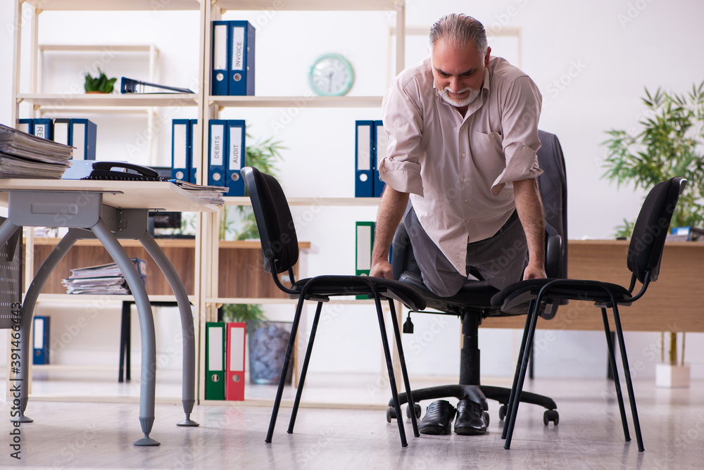 Old male employee doing physical exercises at workplace Old male employee doing physical exercises at workplace
